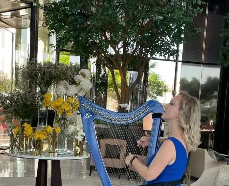Harpist in a blue dress playing a blue harp worn on a strap in a hotel lobby