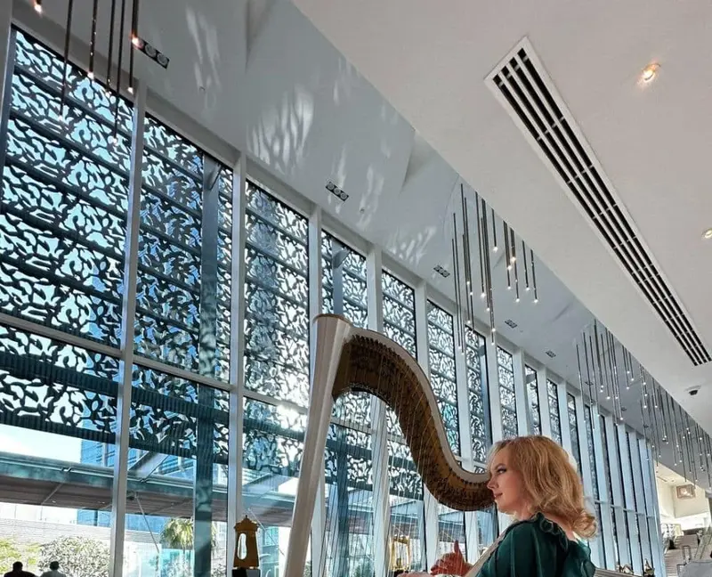 Harpist in a green gown playing a white harp in a bright hotel lobby