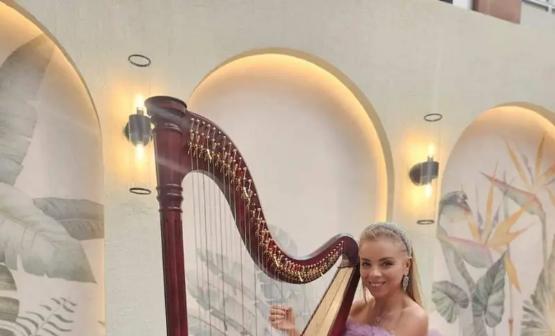 Harpist in a lilac gown smiling beside a wooden concert harp in a bright villa