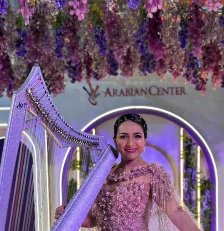 Harpist in a pink gown holding a sparkling silver harp on a floral gala stage