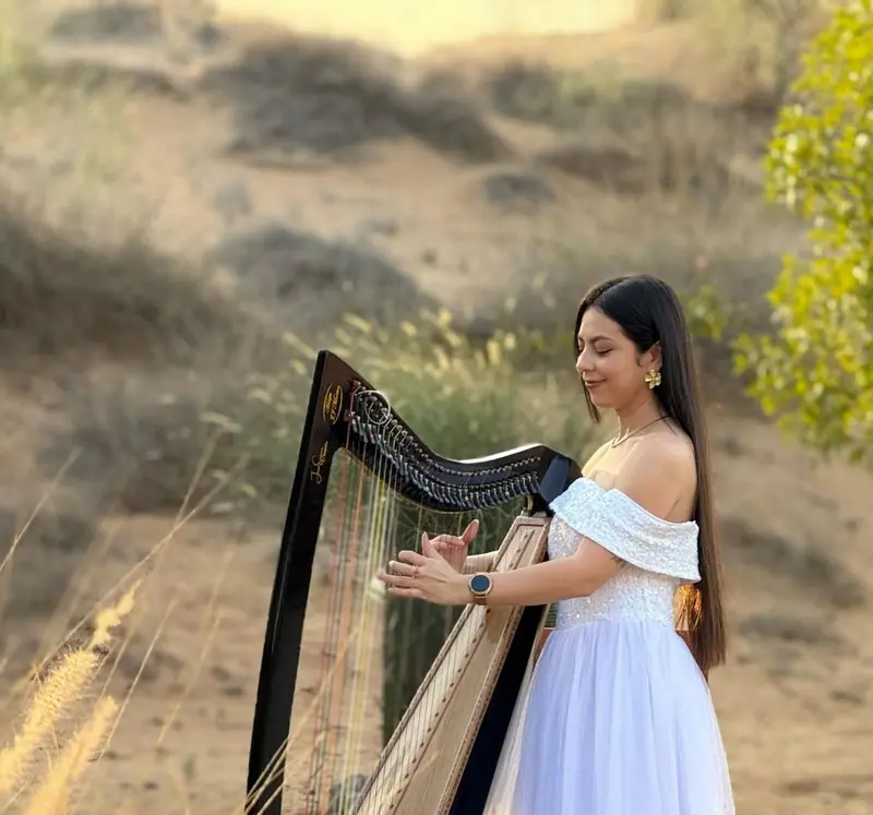 Harpist in a white gown playing a harp outdoors among tall desert grasses