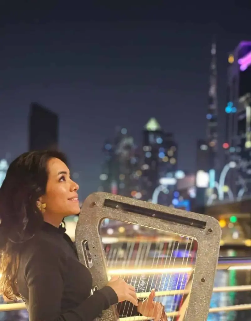 Harpist with a sparkling harp on a terrace at night with city lights behind