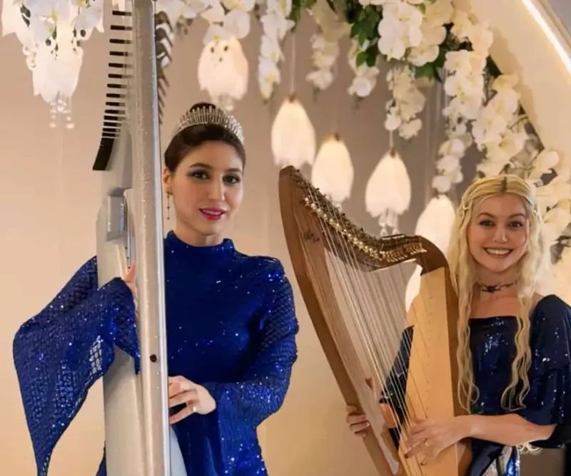 Two harpists in blue gowns standing with their harps at an event