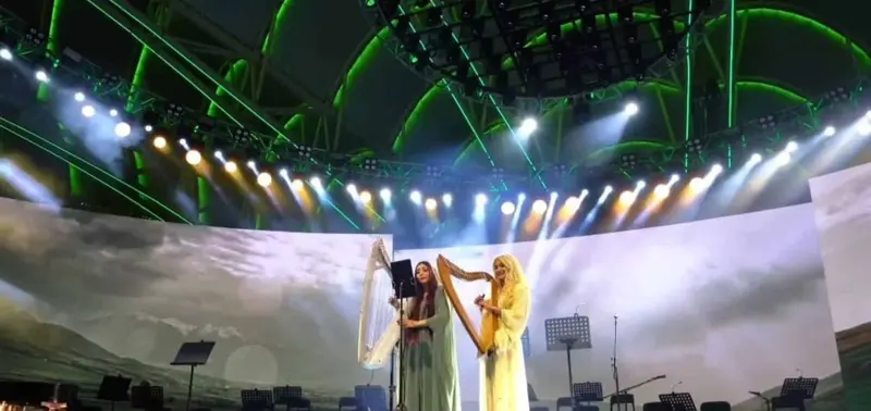 Two harpists performing together on a large lit stage