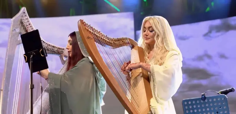 Two harpists playing side by side on a concert stage